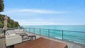 A deck with outdoor seating, a table, and a view of the ocean.
