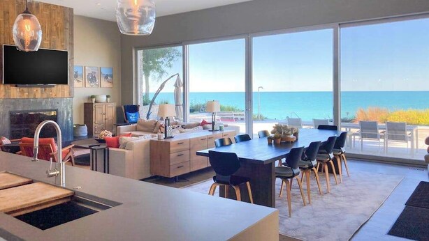 A modern kitchen with a dining area, large windows, and a view of the ocean.