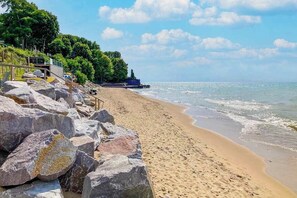 A beach with large rocks, a wooden staircase, and a pier extending into the water. - Large, dog-friendly lakefront home with private pool & hot tub, central AC & W/D (New Buffalo)