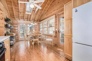 Interior de una cabaña de madera con cocina, comedor y ventanas grandes.