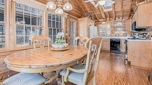 A wooden interior with a round dining table, chairs, a ceiling fan, and a kitchen area. - Calming Cottage on the River W/ Furnished Porch, Lofted Layout & Ideal Location (Saugatuck)