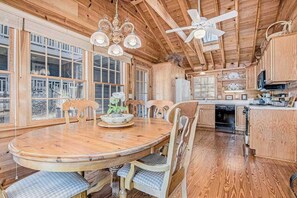 Un interior de madera con una mesa redonda para comer, sillas, un ventilador de techo y una zona de cocina.