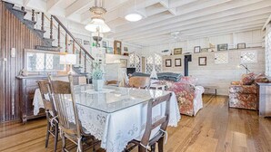 A spacious room with a wooden staircase, a dining table with chairs, a sofa, and a ceiling fan. - Calming Cottage on the River W/ Furnished Porch, Lofted Layout & Ideal Location (Saugatuck)
