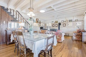 Amplia habitación con una escalera de madera, una mesa de comedor con sillas, un sofá y un ventilador de techo.