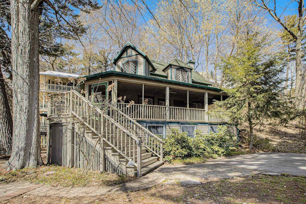 A two-story wooden house with a porch, a staircase, and a fenced yard.