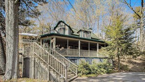 A two-story wooden house with a porch, a staircase, and a fenced yard. - Calming Cottage on the River W/ Furnished Porch, Lofted Layout & Ideal Location (Saugatuck)