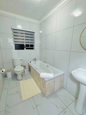 A bathroom with a toilet, bathtub, sink, and a window with blinds.