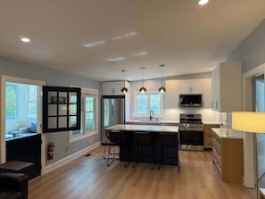 A modern kitchen with a central island, pendant lights, and a large window.
