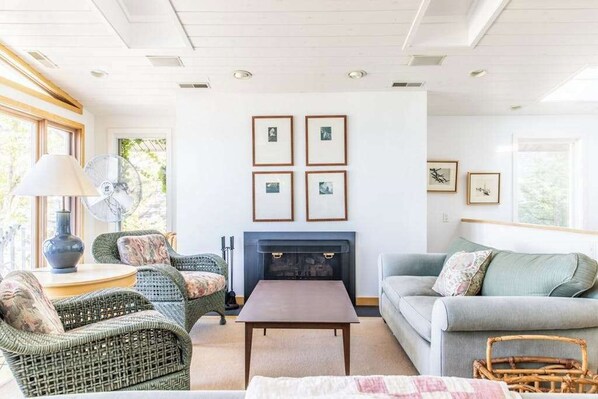 A living room with wicker furniture, a fireplace, and framed pictures on the wall.