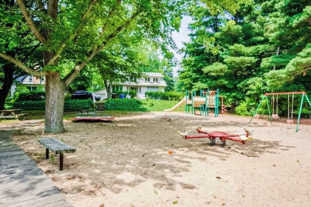 A playground with swings and a slide, surrounded by trees and a bench.