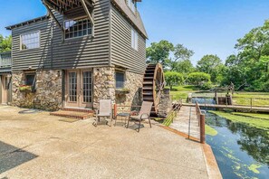 A two-story house with a stone facade, a wooden water wheel, and a dock extending into a pond.