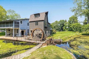 A house with a water wheel and a dock extending into a pond.