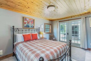 A bedroom with a bed, a painting, a window, and a door.