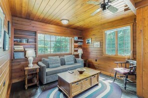 A cozy cabin interior with wooden walls, a sofa, a coffee table, and a chair.