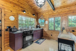 A wooden cabin interior with a kitchen, large windows, and a ceiling light fixture.
