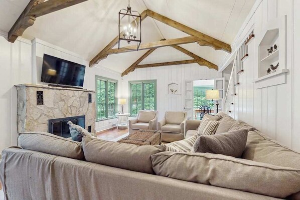 A living room with a stone fireplace, a television, a sofa, and a chandelier. - Stunning Harbor County Home w/ Hot tub, Large yard, Near Beaches & Town. (Michiana)
