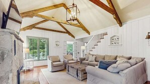Un vaste salon doté d’un haut plafond, de poutres apparentes en bois, d’une cheminée et d’un escalier menant à un autre niveau.