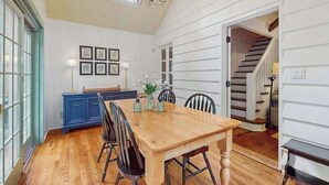 Un coin repas avec une table et des chaises en bois, un buffet bleu et des œuvres d’art encadrées accrochées au mur.