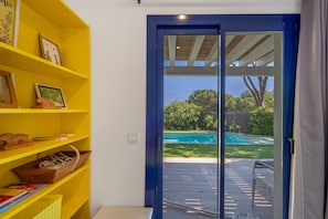 Ein Zimmer mit einem gelben Regalschrank und einer Schiebetür, die in einen Garten mit Pool führt.