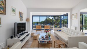 Un salon moderne avec un téléviseur, un canapé, des fauteuils et une grande fenêtre donnant sur un beau paysage.