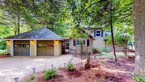 A two-story house with a garage, surrounded by trees and a landscaped garden. - Lake Michigan Retreat with large patio, gas grill, fire pit, & outdoor hot tub (Fennville)