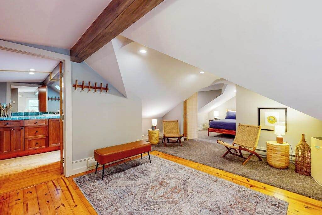 Ein Schlafzimmer im Loft-Stil mit Holzboden, einer Bank, zwei Stühlen, einem kleinen Tisch und einem Bett.