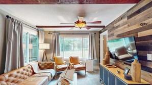 A modern living room with a leather sofa, armchairs, a TV, and a ceiling fan. - Lake Michigan Retreat with large patio, gas grill, fire pit, & outdoor hot tub (Fennville)