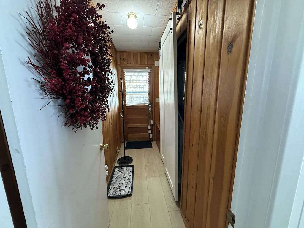 A narrow hallway with wooden walls, a door on the right, and a small mat on the floor.