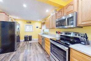 A kitchen with wooden cabinets, a stainless steel refrigerator, a microwave, and an oven. - Charming in Town Home w/ Backyard Patio, Fire Pit, just steps from Indian River! (Indian River)