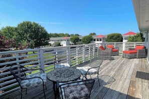 Une terrasse extérieure couverte, avec des tables et des chaises, une clôture blanche et, au fond, des bâtiments aux toits rouges.