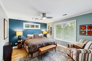 Une chambre à coucher comprenant un lit, un banc, une chaise, un ventilateur de plafond et des œuvres d’art accrochées aux murs.
