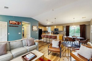 A modern living room with a sofa, coffee table, and a dining area with chairs and a table. - Stylish dog-friendly retreat with furnished deck, pool, & firepits (Douglas)