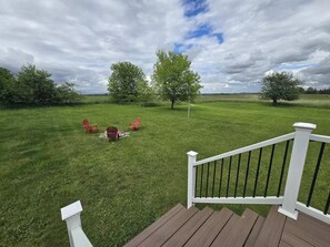 Eine Terrasse mit weißer Reling, die auf eine grüne Fläche mit Bäumen und Gartenmöbeln blickt.