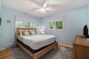 Un dormitorio con cama, ventilador de techo, escritorio y ventanas.