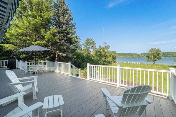 Une terrasse avec des chaises Adirondack blanches, une table et un barbecue.