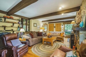 A cozy living room with a fireplace, leather furniture, and a bookshelf. - Terrific riverfront home near the slopes w/ firepit, free WiFi & five-acre lot (Thompsonville)