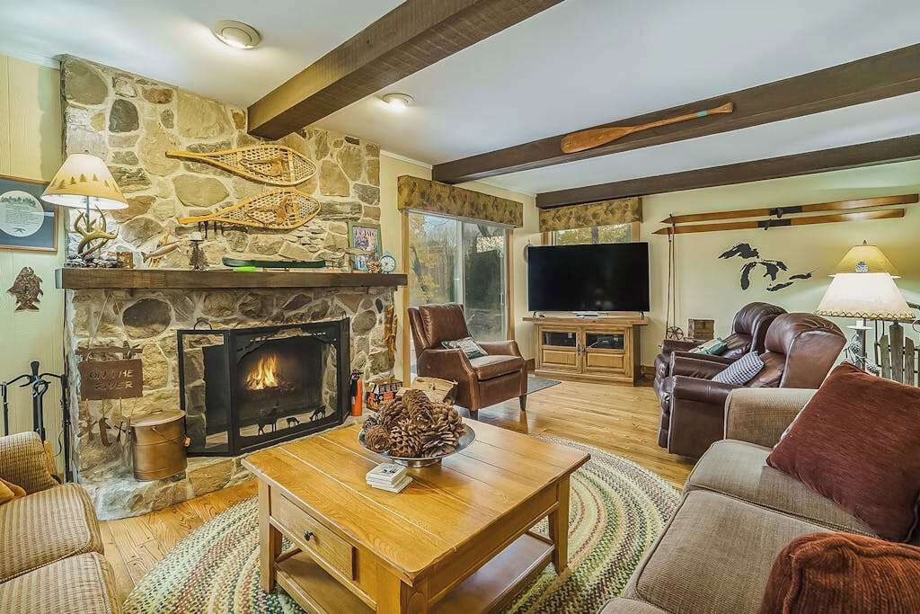 Un salon chaleureux avec une cheminée en pierre, des meubles en bois, un téléviseur et un coin salon confortable.