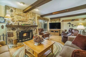 A cozy living room with a stone fireplace, wooden furniture, a television, and a comfortable seating area. - Terrific riverfront home near the slopes w/ firepit, free WiFi & five-acre lot (Thompsonville)
