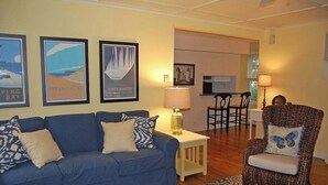 Ein Wohnzimmer mit einem blauen Sofa, einem gemusterten Sessel, einem kleinen Tisch mit einer Lampe und gerahmten Bildern an der Wand.