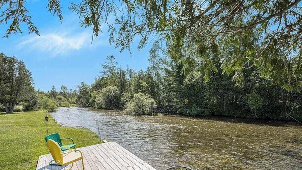 Eine Holzterrasse mit Stühlen mit Blick auf einen Fluss, umgeben von Bäumen.