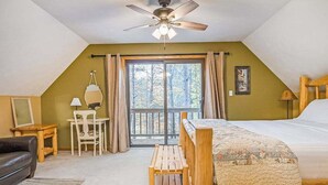 Un dormitorio con cama, ventilador de techo, escritorio, silla y ventana con vista a  árboles.