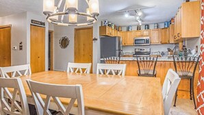Un comedor con una mesa de madera y sillas blancas, una cocina con armarios de madera y electrodomésticos, y una araña.