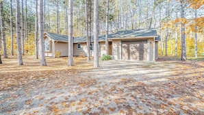 A single-story house with a garage, surrounded by a forest with tall trees and fallen leaves. - Stunning home w/ golf course views plus private deck near resort amenities (Thompsonville)