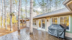 A wooden deck with a covered grill, a house with sliding glass doors, and a forested background. - Stunning home w/ golf course views plus private deck near resort amenities (Thompsonville)
