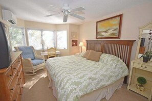 Un dormitorio con cama, una silla, cómoda y ventilador de techo, además de un cuadro en la pared.