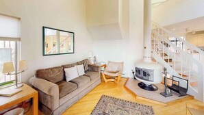 Een moderne woonkamer met een bank, een fauteuil, een tafel met lampen, een ingelijst schilderij en een opvallende witte spiltrap.