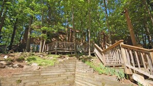 Un escalier en bois mène à une maison entourée d’arbres.