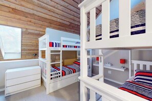 A bunk bed room with a wooden ceiling, a window, and a white dresser.