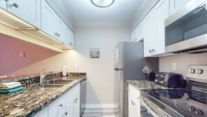 A compact kitchen with white cabinets, a granite countertop, a stainless steel stove, and a refrigerator. - River-view townhouse with Lake Michigan access, deck, fireplace, and cable (Glen Arbor)