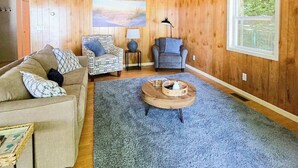 A living room with a sofa, two chairs, a coffee table, a painting, and a window. - Glen Lake Home w/private beach frontage and dock (Empire)